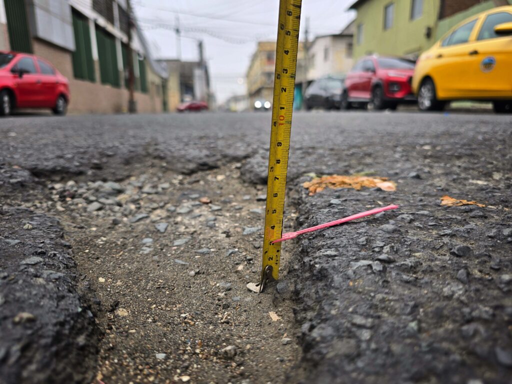 Un metro y una trincheta de plástico señalan los 3 centímetros de profundidad de un bache de la calle General Francisco Robles, en el barrio Cuba, en Guayaquil, Ecuador. Fotografía: Karol E. Noroña